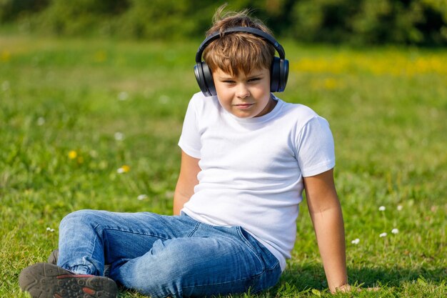 Jongen met koptelefoon die naar muziek luistert terwijl hij op het gras in het park zit