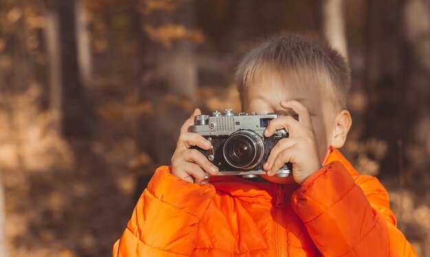 Jongen met retro camera fotograferen buiten in de herfst natuur. Vrije tijd en fotografen concept