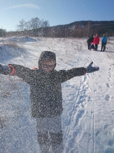 Foto jongen met uitgestrekte armen speelt met sneeuw op het veld tegen de lucht