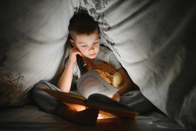 Jongen met zaklamp leesboek onder deken thuis