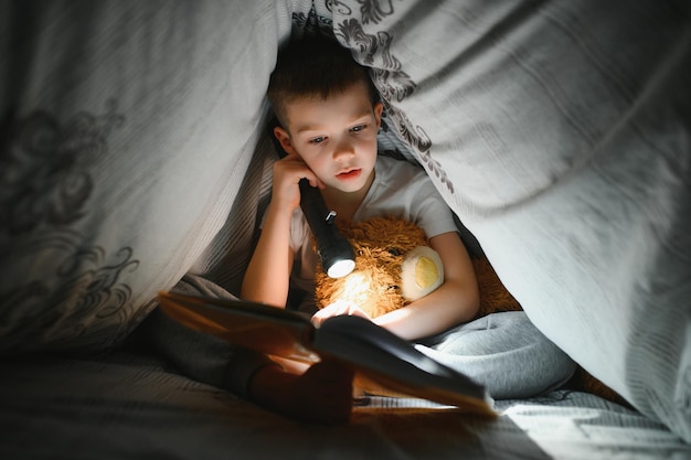 Jongen met zaklamp leesboek onder deken thuis