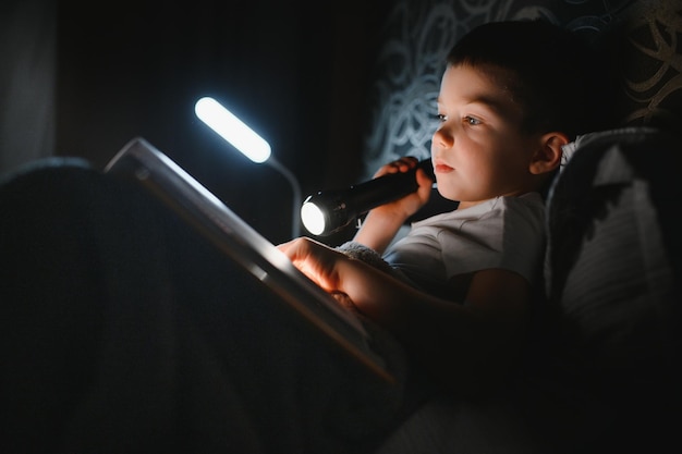 Jongen met zaklamp leesboek onder deken thuis