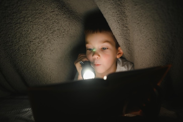 Jongen met zaklamp leesboek onder deken thuis