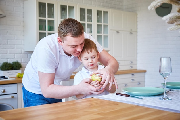 Jongen met zijn vader in de keuken. Het kind eet een appel. Het concept van familie en vaderschap.