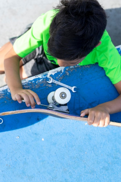 Jongen repareert het wiel van zijn skateboard nadat hij het op een zonnige dag in het skateboardpark heeft gebruikt.