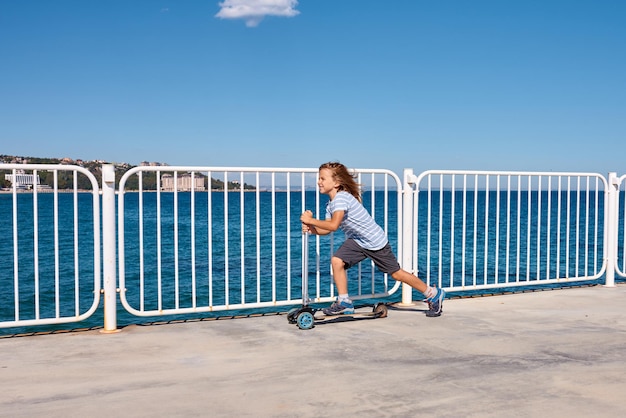 Jongen rijdt op een scooter op een pier op een zonnige dag