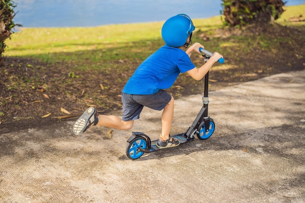 Jongen rijdt op scooters buiten in het park in de zomer Kinderen spelen graag buiten