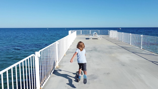 Jongen rijdt scooter op een pier op sunyday