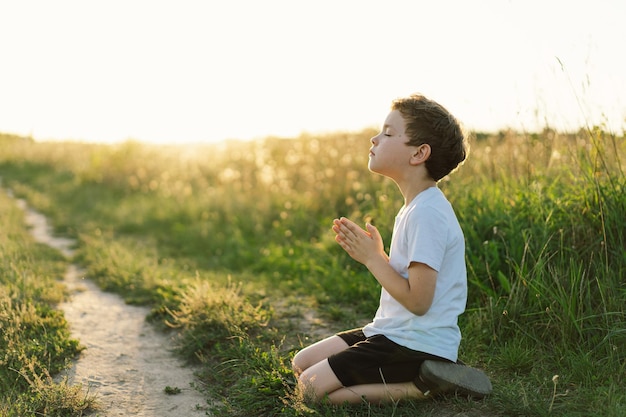 Jongen sloot haar ogen en bad in een veld bij zonsondergang Handen gevouwen in gebedsconcept voor geloofsspiritualiteit en religie