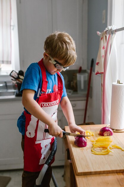 Foto jongen snijdt uien in de keuken thuis.