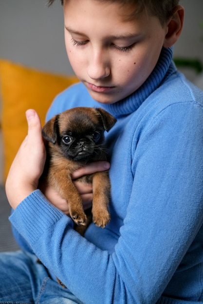 Jongen speelt met babyhond. Kid spelen met puppy thuis. Kleine jongen en griffon of brabanson hond