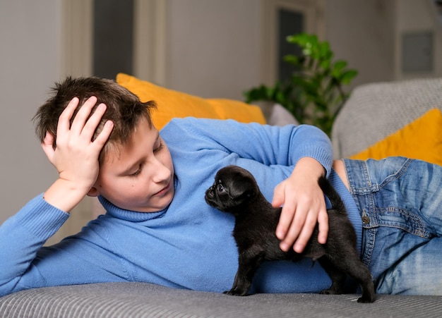 Jongen speelt met babyhond. Kid spelen met puppy thuis. Kleine jongen en griffon of brabanson hond