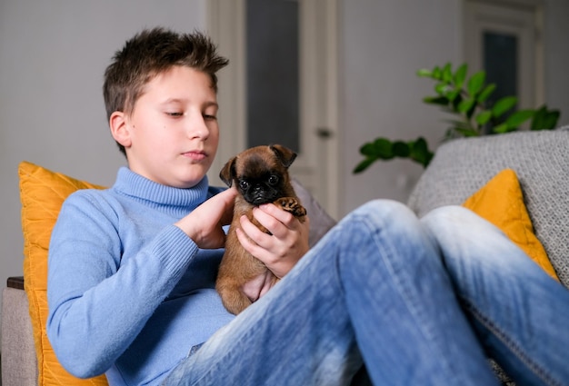 Jongen speelt met babyhond. Kid spelen met puppy thuis. Kleine jongen en griffon of brabanson hond