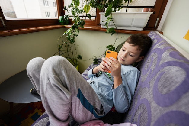 Jongen speelt telefoon op de bank op het balkon