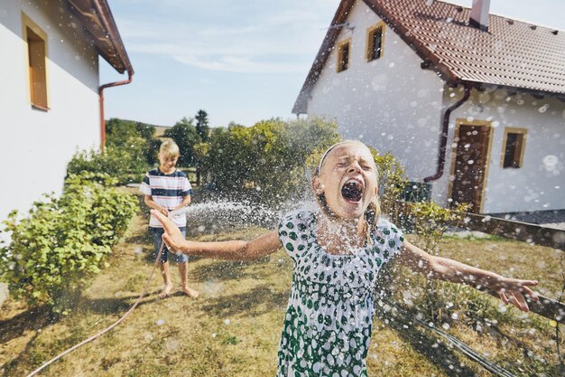 Jongen spuit water op zus die in de tuin staat.