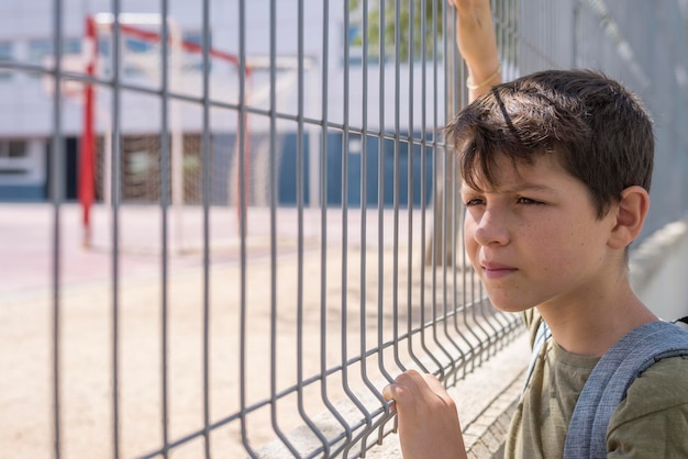 Jongen staat bij het hek op het schoolplein.
