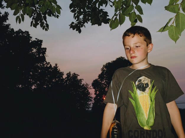 Foto jongen staat tegen bomen bij zonsondergang