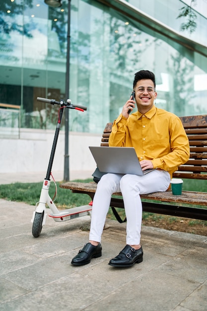 Jongen studeert in een park met een laptop en een scooter