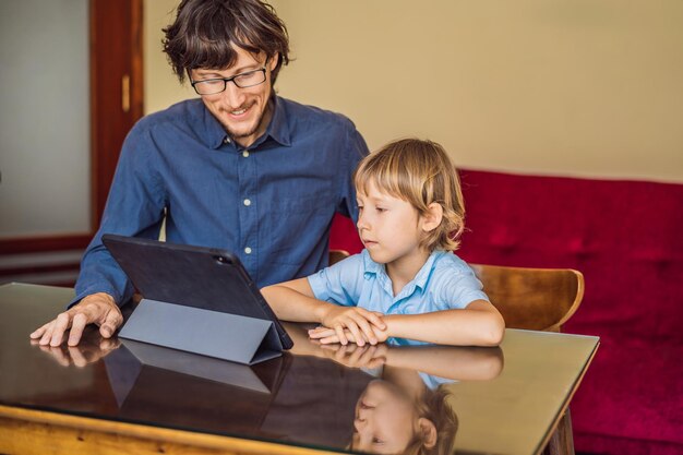 Jongen studeert thuis online met behulp van een tablet Vader helpt hem te leren Studeren tijdens quarantaine Wereldwijd pandemisch covid19-virus