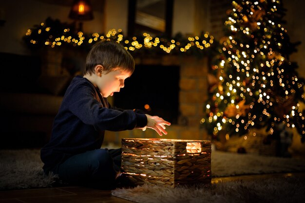 Jongen van 5-7 jaar opende een wonderlijk nieuwjaarscadeau in een kerstinterieur met een kerstboom