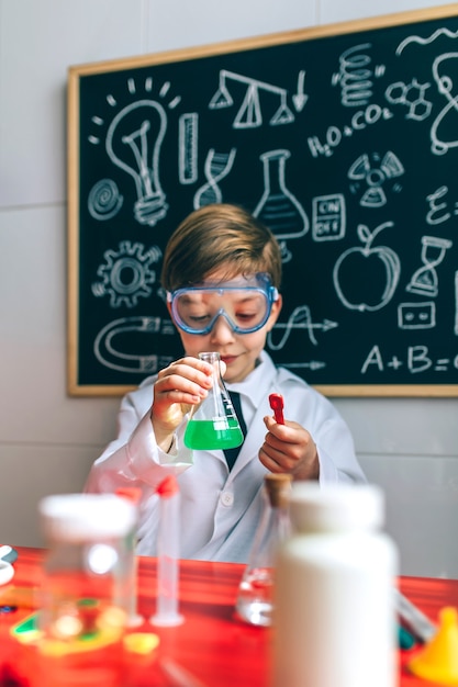 Jongen verkleed als scheikundige spelen met scheikundespel voor een schoolbord met tekeningen