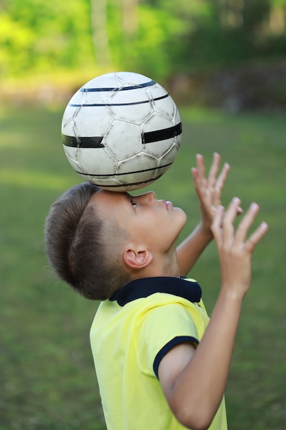 Jongen voetballer in een geel t-shirt staat op het voetbalveld met een bal op zijn hoofd.