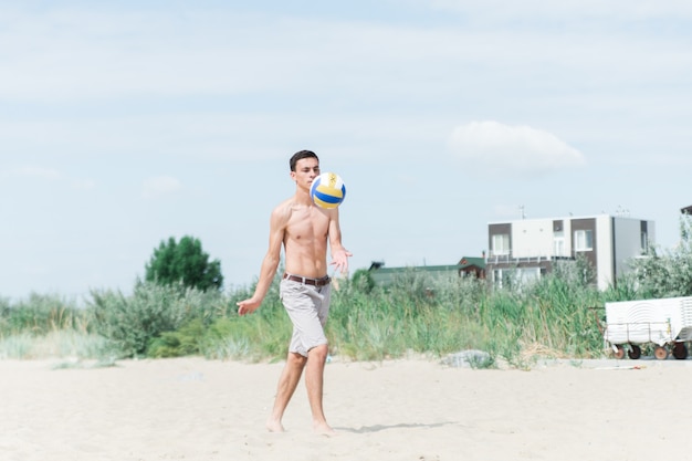jongen volleyballen op het strand. de man zonder shirt serveert de bal.