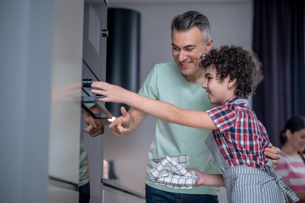 Jongen zijwaarts naar camera die oven aanraakt en vader kijkt