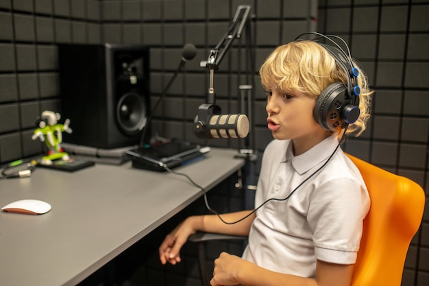 Jongen zit aan het bureau en praat in de microfoon