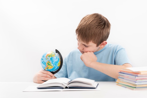 Jongen zit aan tafel met globe in handen en denkt aan iets Student doet huiswerk en bekijkt globe zorgvuldig