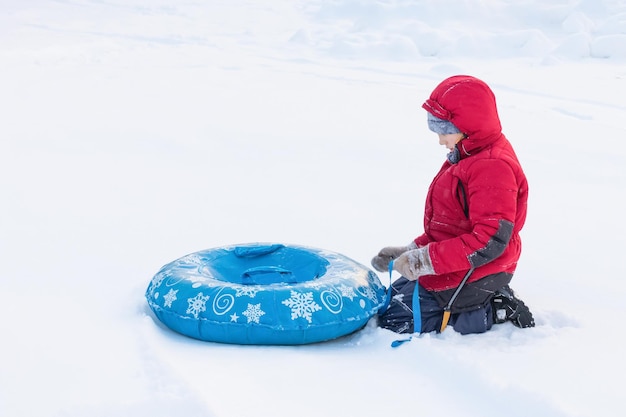 Jongen zit met blauwe buizen op sneeuw in winterkleren