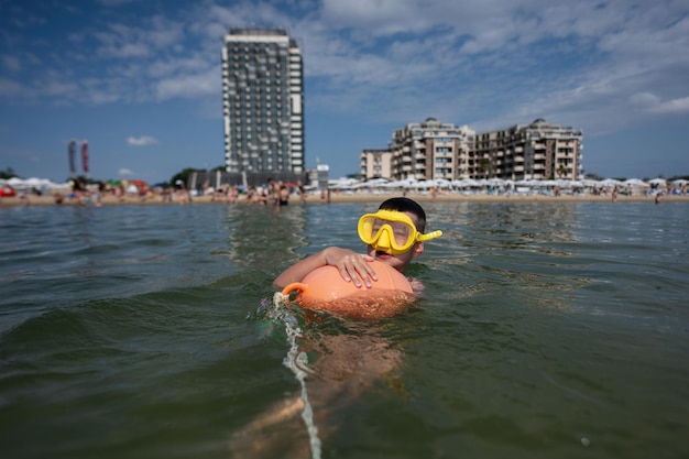 Jongen zwemmen in de zee met oranje boei en duikbril