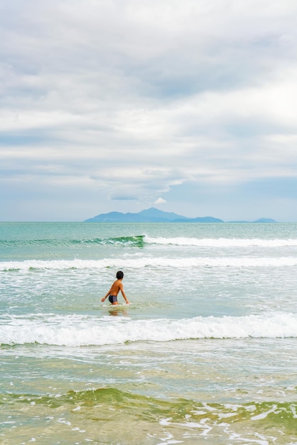 Jongen zwemmen in de zee op het China Beach in Danang in Vietnam. Het wordt ook Non Nuoc Beach genoemd. Zuid-Chinese Zee en Marble Mountains op de achtergrond.