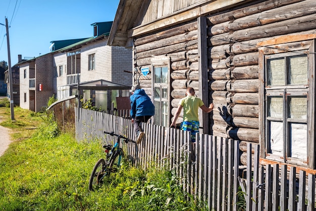 Jongens achter het hek van een houten huis op de Solovetsky-eilanden en een fiets