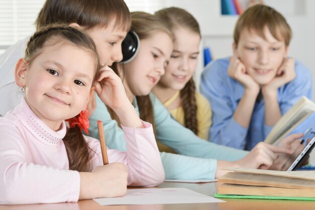 Jongens en meisjes maken samen huiswerk aan tafel thuis, een van hen luistert naar een audioboek