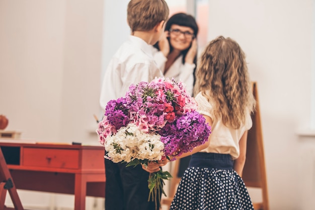 Jongens- en meisjeskinderen geven bloemen als leraar op school in de dag van de leraar