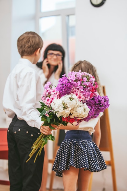 Jongens- en meisjeskinderen geven bloemen als leraar op school in de dag van de leraar