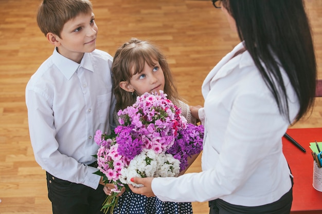 Jongens- en meisjeskinderen geven bloemen als onderwijzeres op school