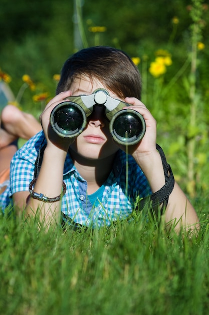 Jongens jonge onderzoeker die met verrekijkersmilieu onderzoeken in groene tuin