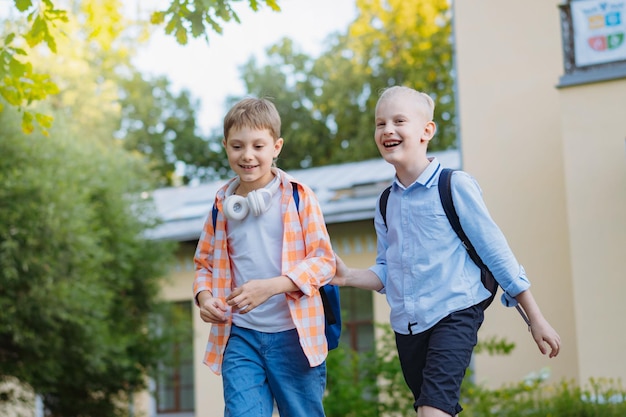 Jongens lopen van school met rugzakken op een zonnige dag voor de deur van de school Begin van het academisch jaar