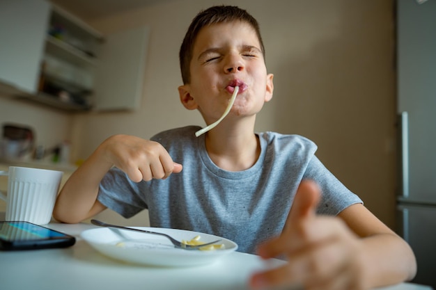 Jongenskind dat macaroni-retractie-lange pasta in zijn mond eet