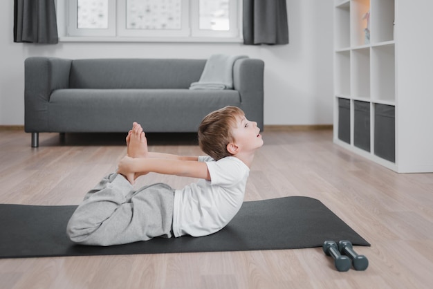 Jongenskind dat yoga-booghouding beoefent en aan het trainen is met een sportkleding-t-shirtbroek