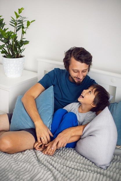 Jongenskind en zijn vader zitten op het bed in de slaapkamer en lachen om een grap