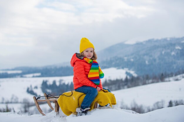Jongenskind glijden met slee in de wintersneeuw kerstvakantie voor kinderen en gelukkig nieuwjaar