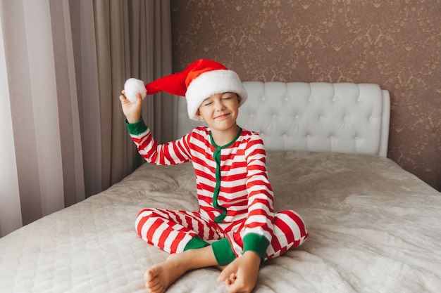 Jongenskind in een kerstmuts en pyjama ligt op een bed met wit beddengoed, nieuwjaar, kerstmis