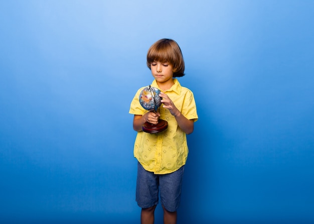 Jongensschooljongen 7 jaar oude schooljongen met een souvenirbol in zijn handen glimlachend op een blauwe achtergrond