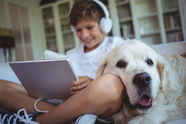 Jongenszitting op bank met huisdierenhond en het luisteren aan muziek op digitale tablet