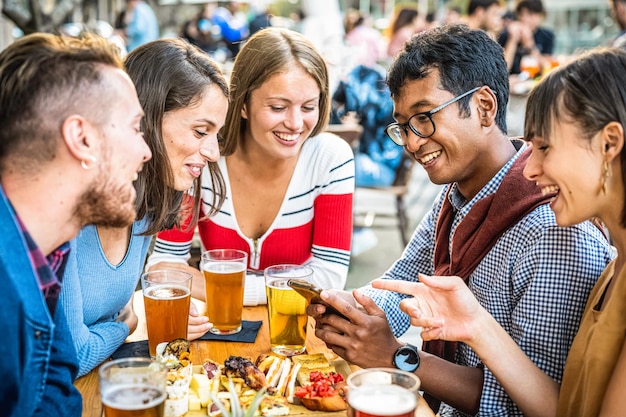 Jongeren die plezier hebben in biercafé millennials mensen die drinken en eten in restaurant jonge studenten die slimme apparaten gebruiken om actief te zijn op sociale media