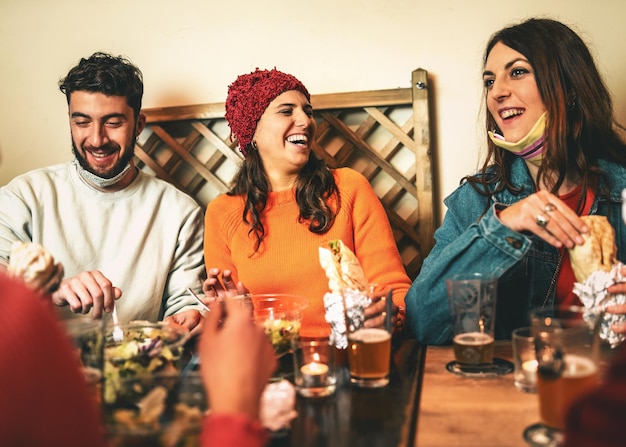 Jongeren met verlaagd coronavirus gezichtsmasker hebben plezier samen eten in een pub - vrienden reünie in een restaurant in covid-19 tijden