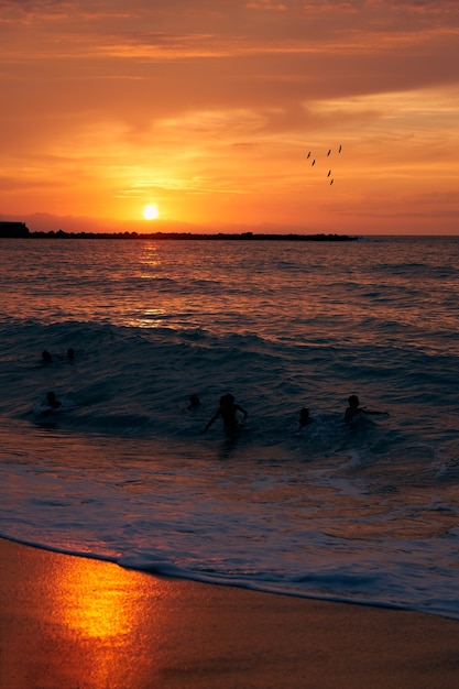 Jongeren spelen met de golven bij zonsondergang